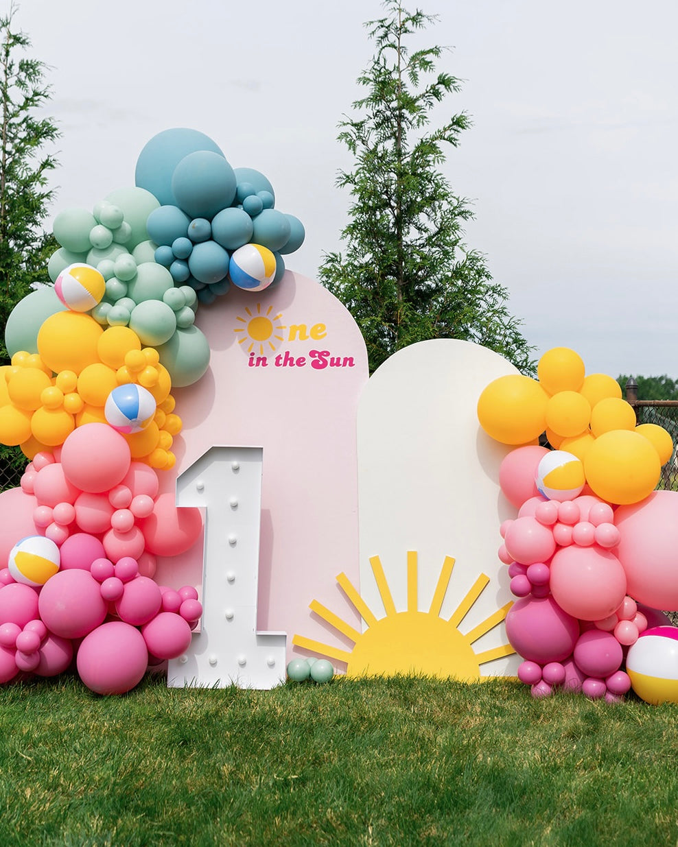 Colorful balloon installation with 'One in the Sun' on two arch backdrop.