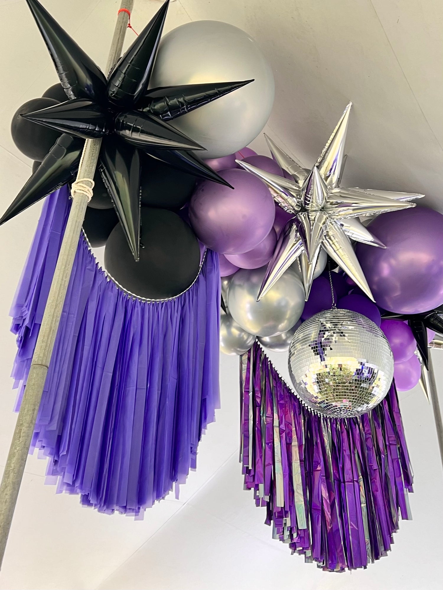 Tent ceiling balloon installation with black, silver, and purple balloons, fringe, and a disco ball.
