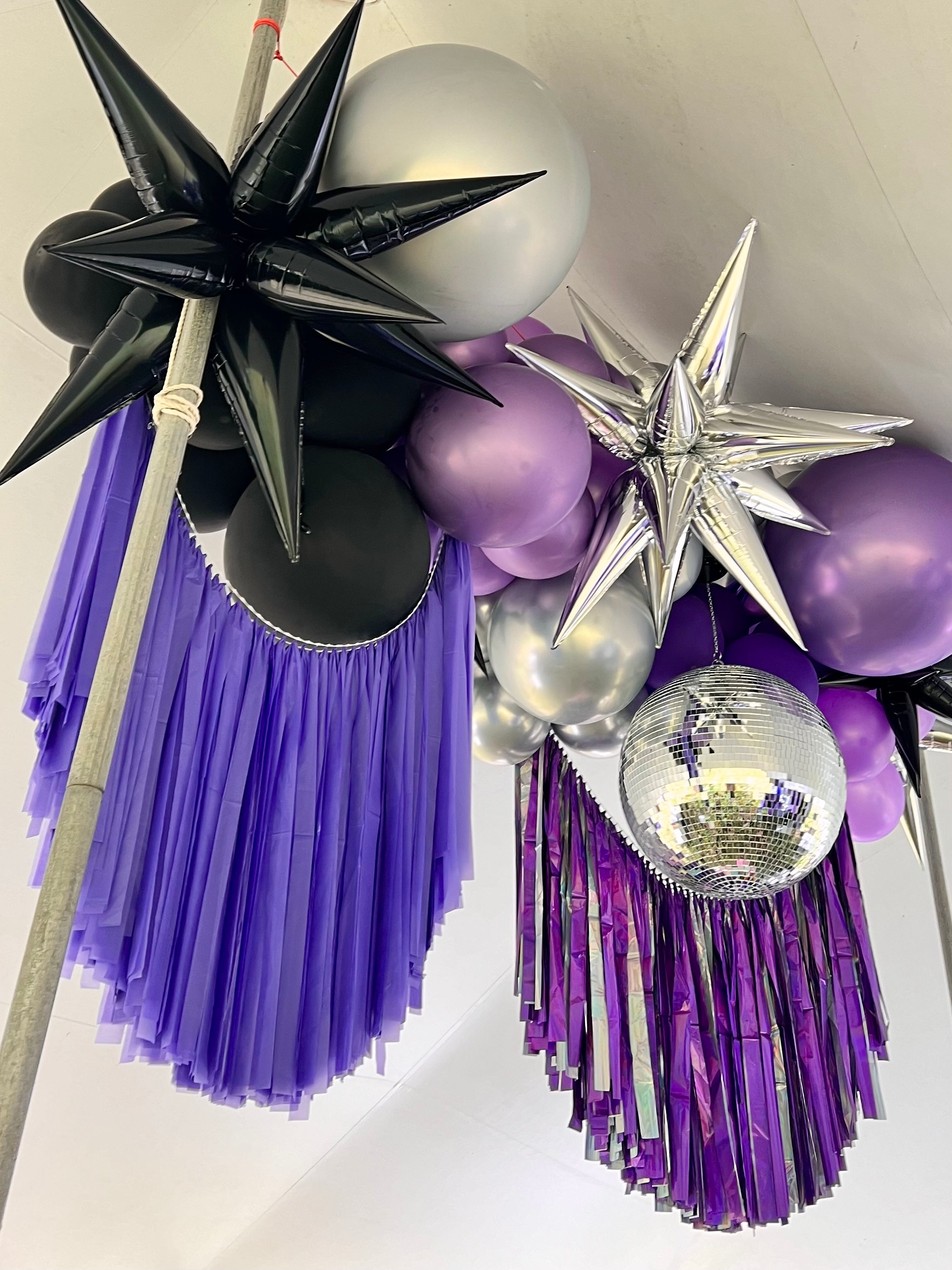 Tent ceiling balloon installation with black, silver, and purple balloons, fringe, and a disco ball.