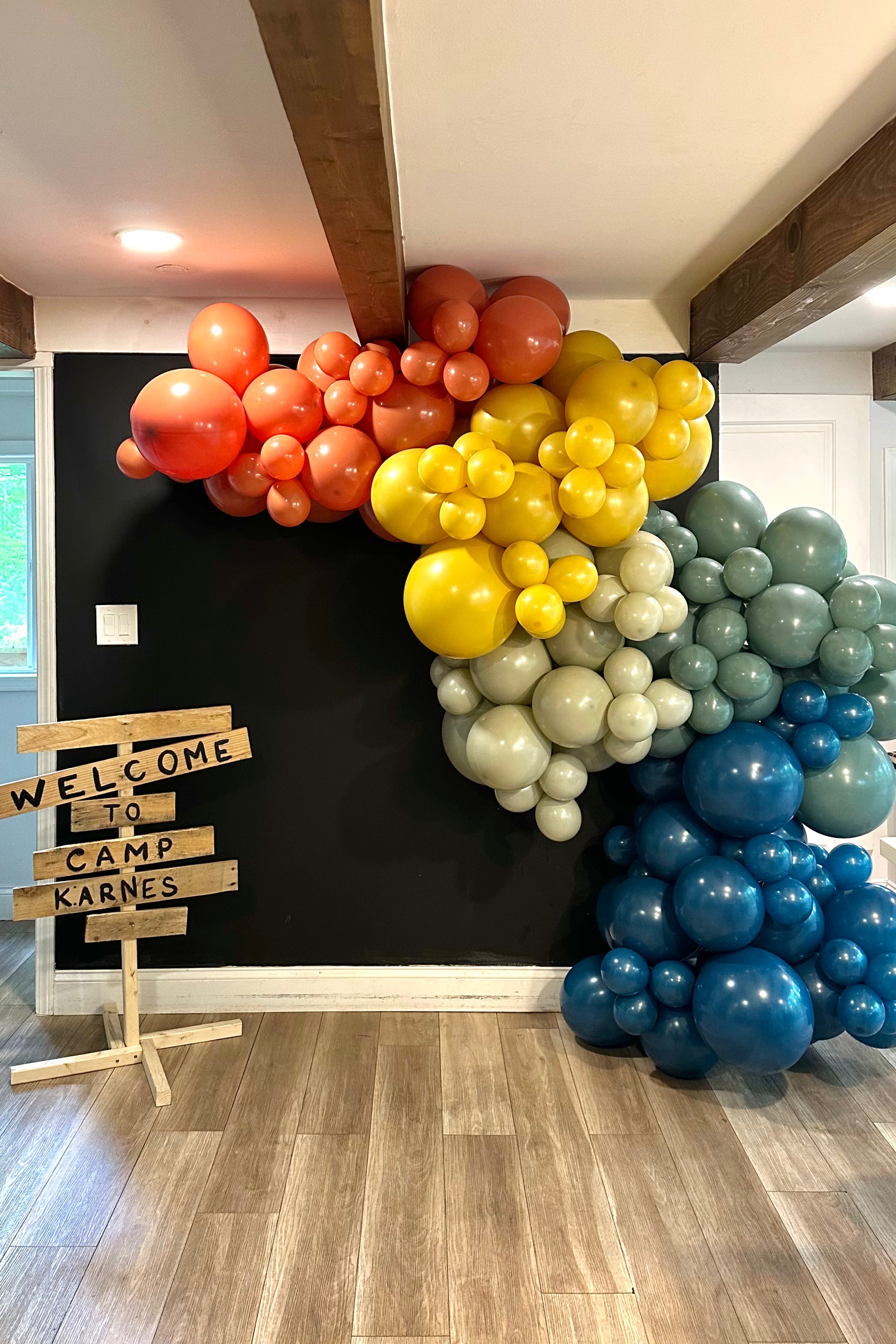 Colorful balloon garland in front of a black wall with custom camp sign.