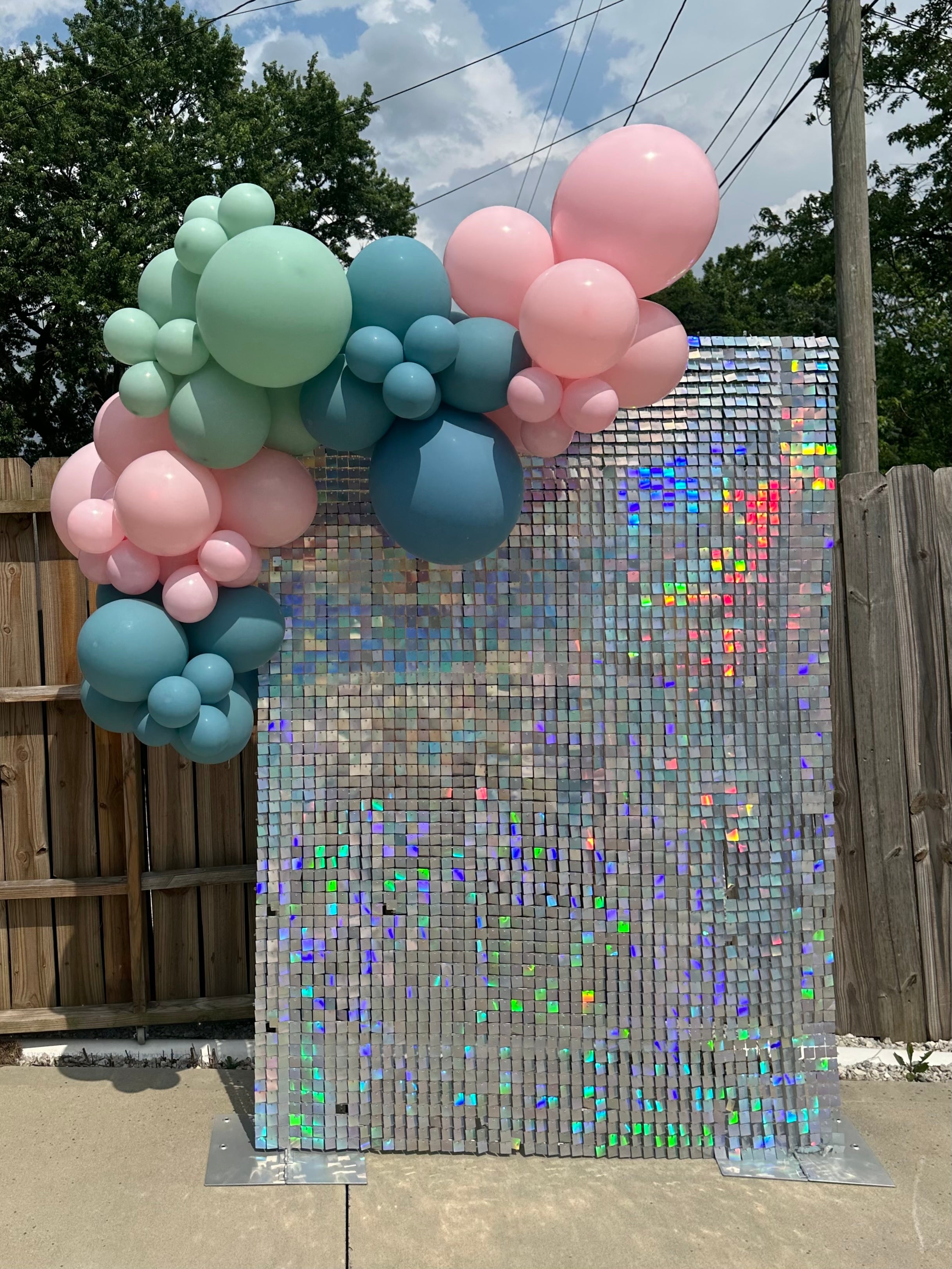 Balloon garland with pink, blue, and green balloons on a silver shimmer wall.